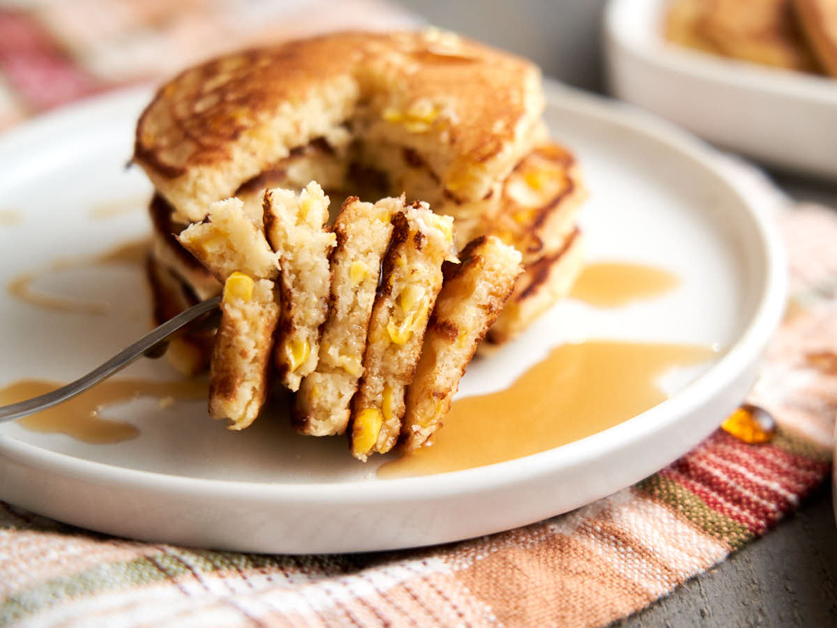 cut stack of corn pancakes on a fork with maple syrup