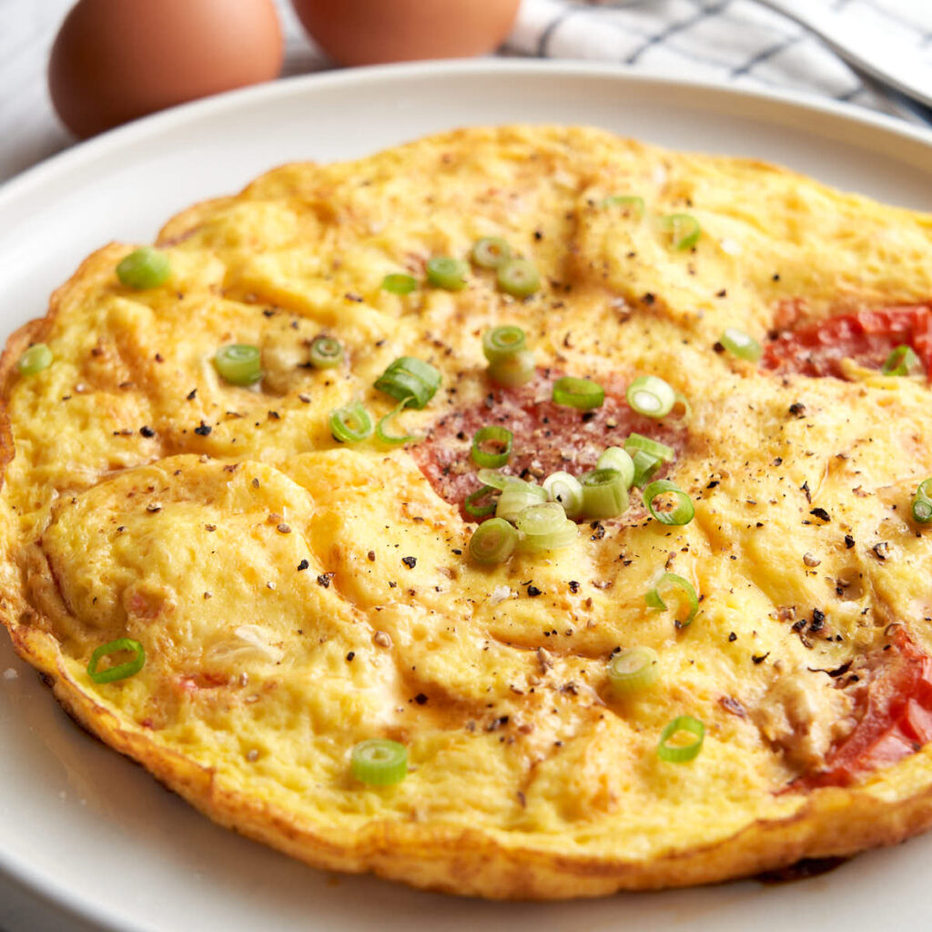 Tomato egg breakfast - round omelette style on a plate. Topped with sesame oil, salt, pepper and green onions.