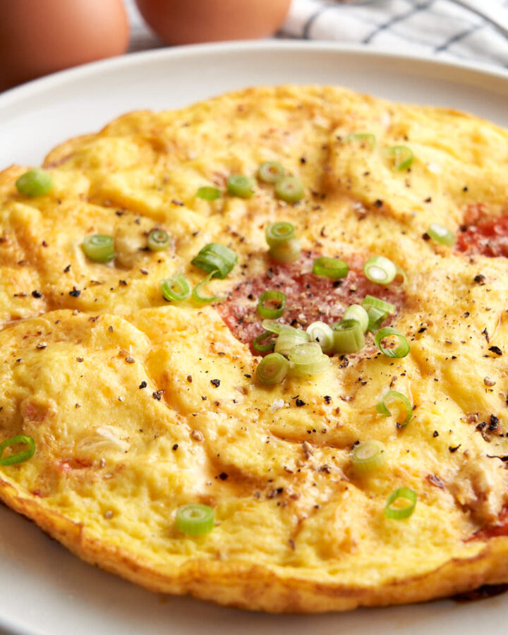 Tomato egg breakfast - round omelette style on a plate. Topped with sesame oil, salt, pepper and green onions.